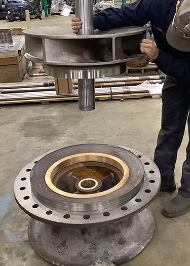 Technician installing a wear band onto a vertical turbine pump bowl, highlighting the importance of proper material selection for pump components.